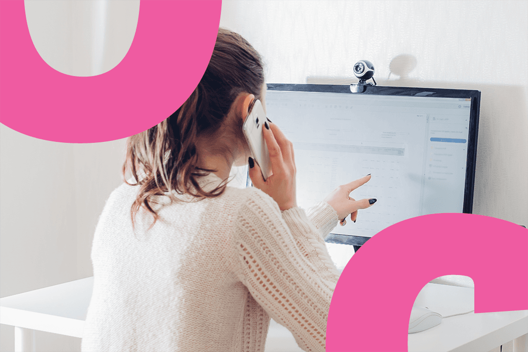 A back of a woman who is talking on the phone and pointing at the computer screen.